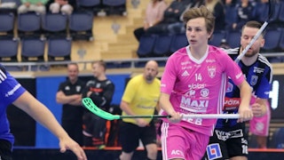 Faluns Malte Lundmark i rosa matchställ till höger i bild. Lundmark håller klubban med båda händer i midjehöjd och bakom honom syns en Siriusspelare och en domare.